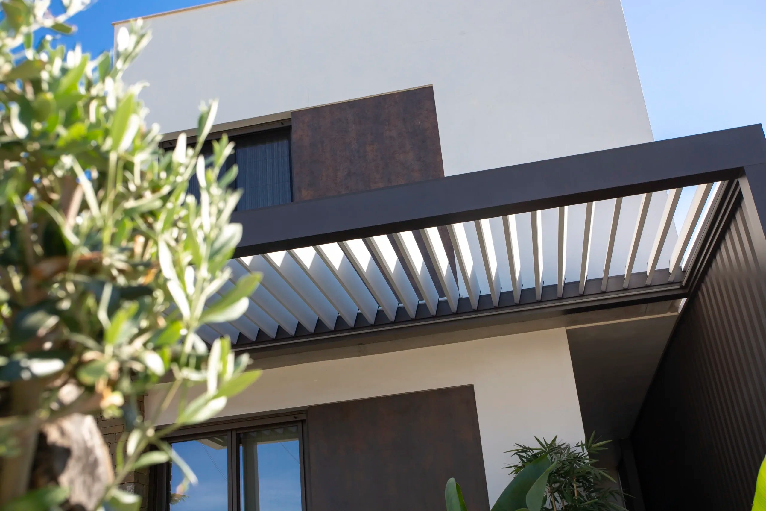 Pérgola bioclimática integrada en vivienda con lateral cubiero y lamas orintables en la parte superior
