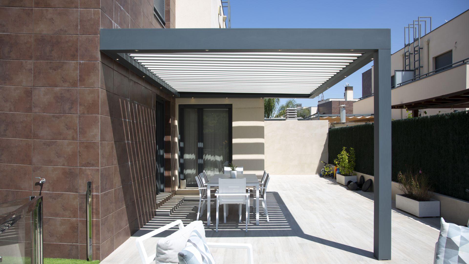 Pérgolas adosada en terraza con pilar de apoyo con sillas y mesa de terraza a la sombra de la pérgola