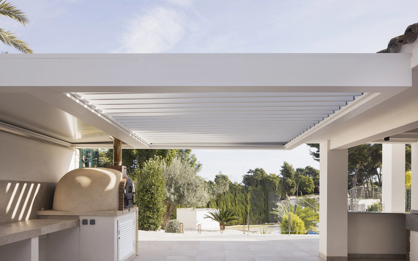 Pérgola de aluminio blanco con lamas movibles adosada entre dos módulos arquitectónicos diferentes creada a medida para ese espacio creada e