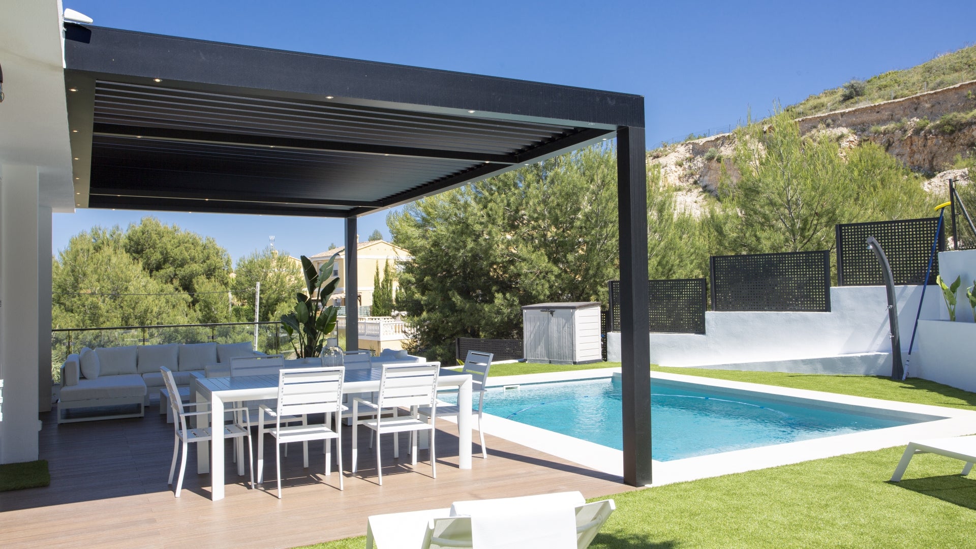 Pergola bioclimática exterior en terraza con piscina, jardín sus sillas y mesa de exterior a la sombra de la Pérgola