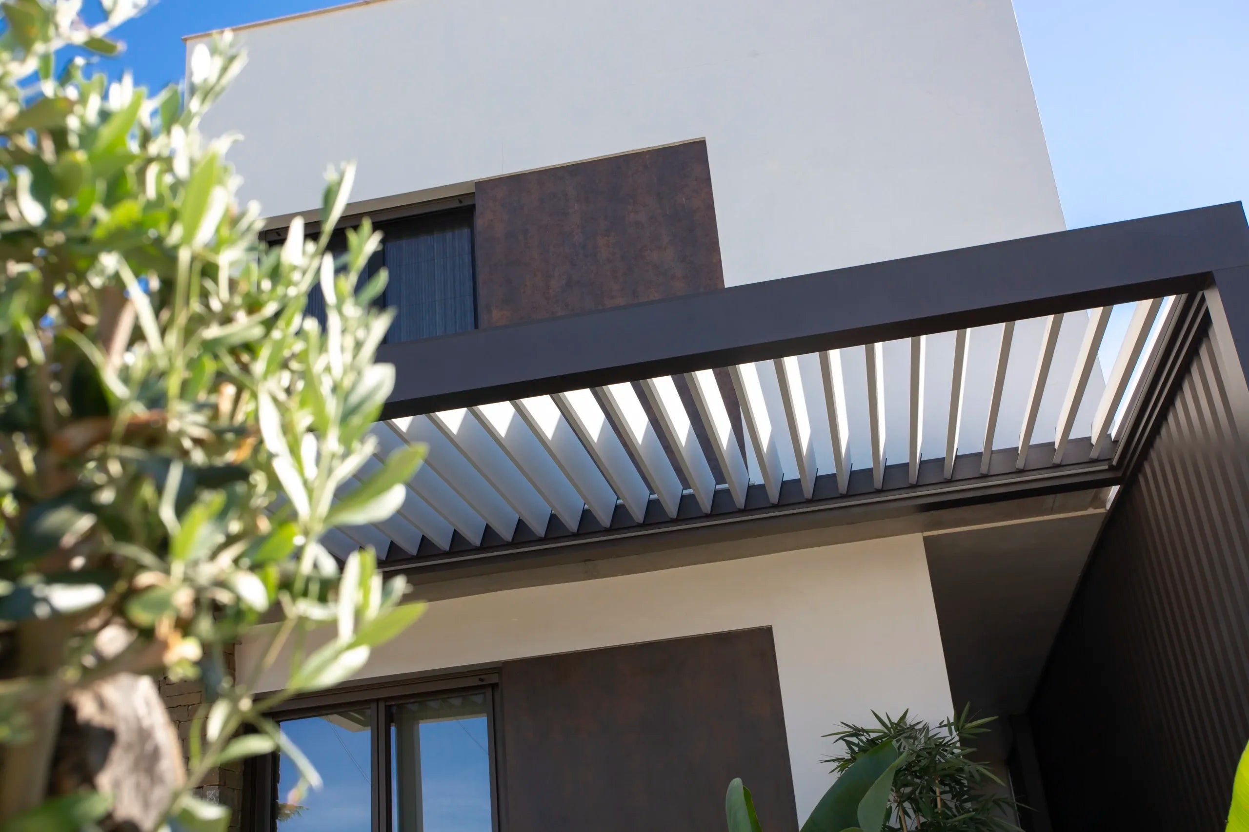 Pérgola bioclimática integrada en vivienda con lateral cubiero y lamas orintables en la parte superior 