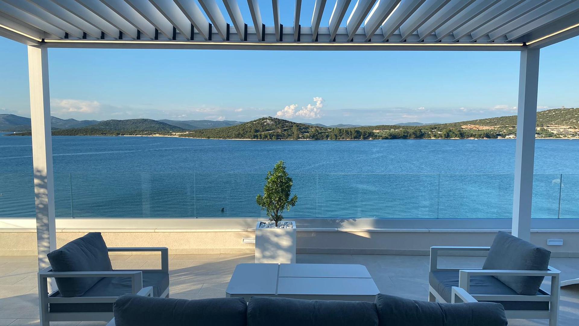 Pérgola dando al mar en una terraza con sofá y sillones de exterior